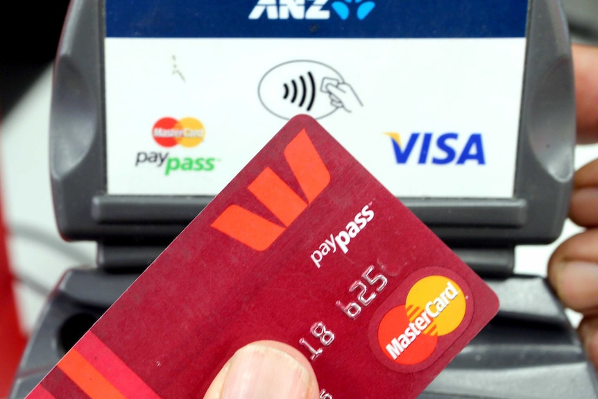 A close-up of a Mastercard, with a paypass machine in the background.