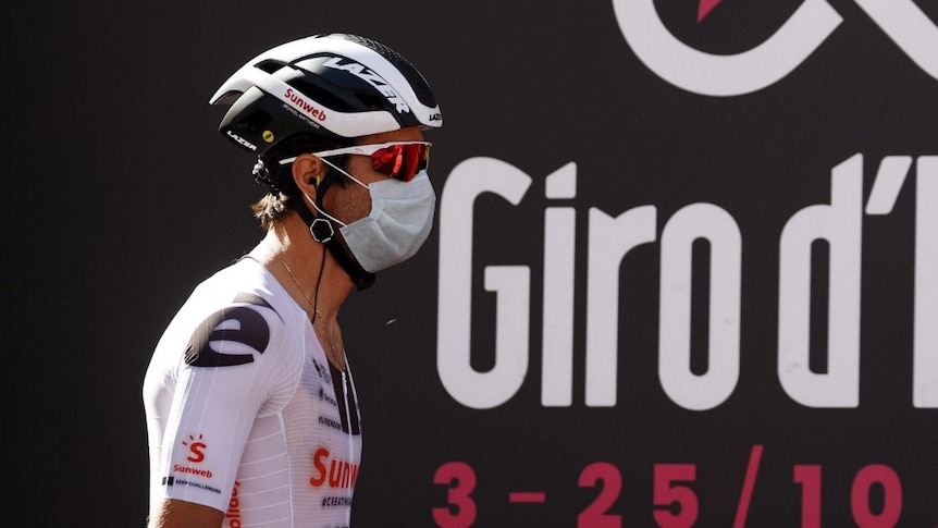 A cyclist in professional gear wears a surgical mask.