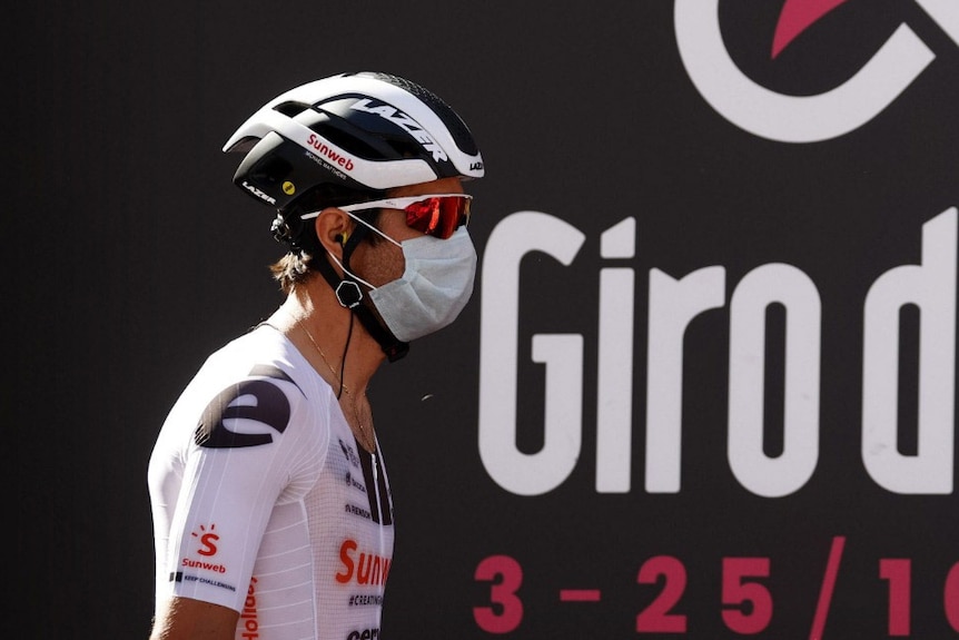 A cyclist in professional gear wears a surgical mask.