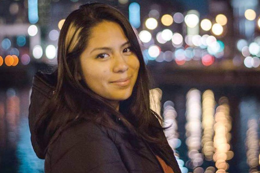 Nohemi Gonzalez stands smiling on a moonlit night with the lights of a city in the background.