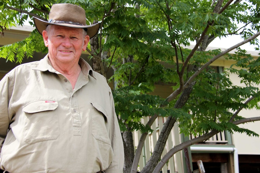 Wan in khaki shirt and bush hat in front of his house