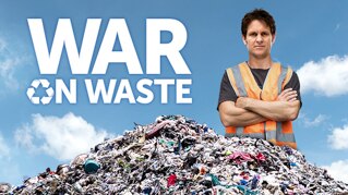 A man in a fluoro orange vest with his arms cross standing behind a pile of rubbish