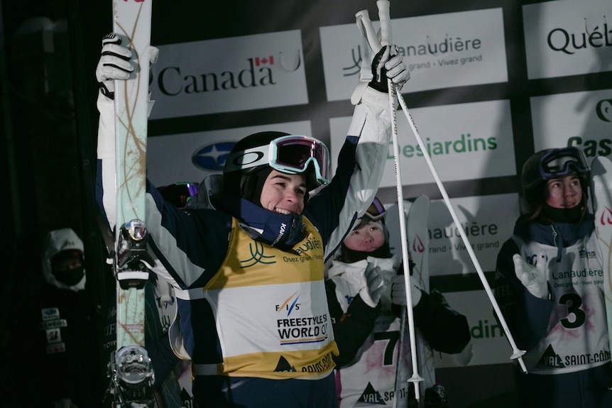 Jakara Anthony holds up her ski poles and skis and smiles