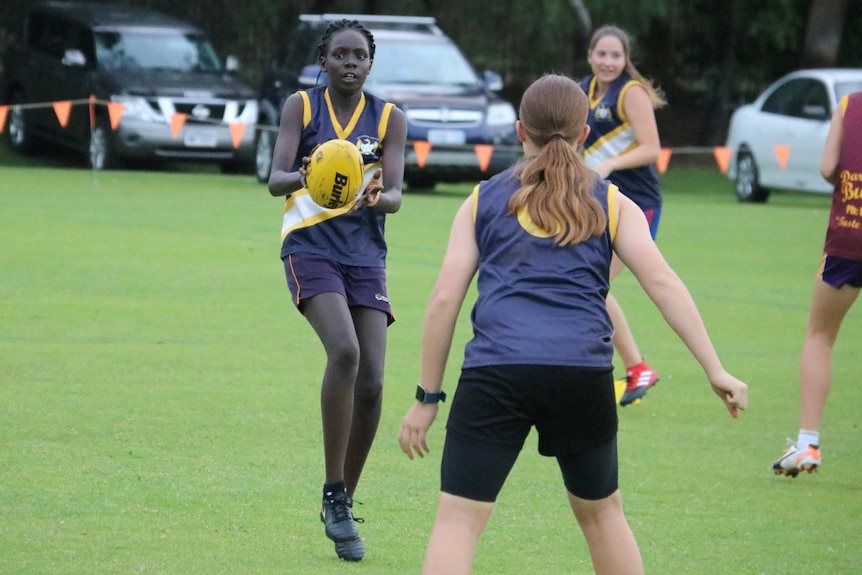 Aker Athoi holds a football on an oval with several other players.