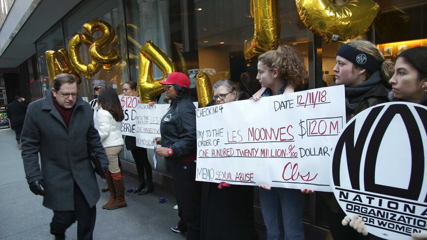 Protesters stand outside the site of  CBS offices brandishing oversized cheques that have disgraced executive Les Moonves listed