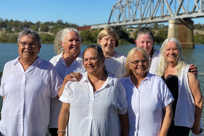 Eight women wearing white shirts stand together in two rows