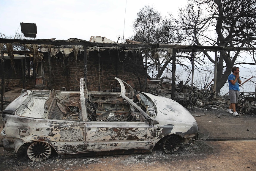 A man reacts next to a burnt car in Mati