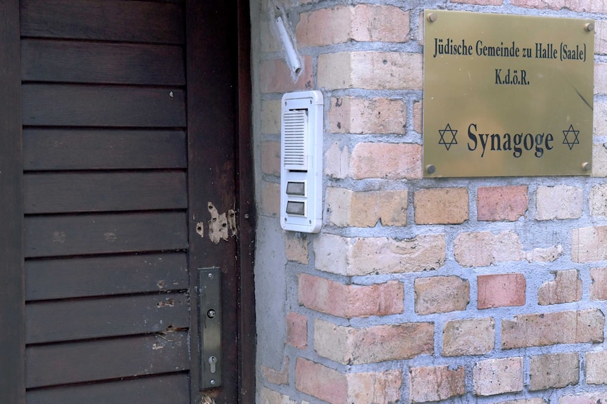 Holes in a wooden door next to a gold plaque that says "synagogue".