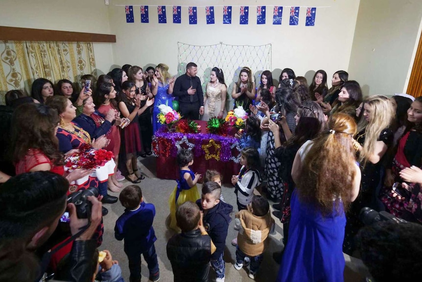 A man and a woman celebrate their engagement in a room with lots of people.