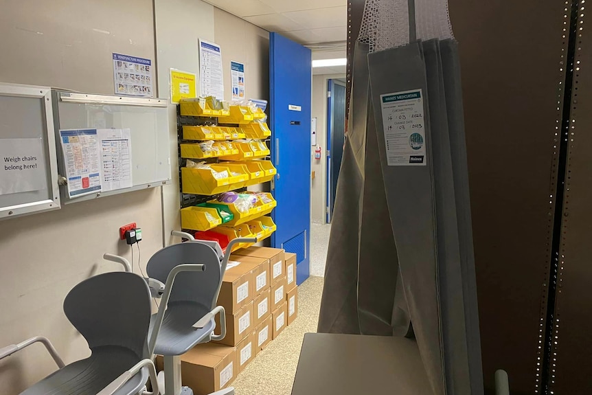 An area with a grey hospital curtain, chairs and boxes and other hospital equipment and items