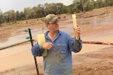 Daniel Hayman stands and holds a rain gauge in the mud at Milray property.