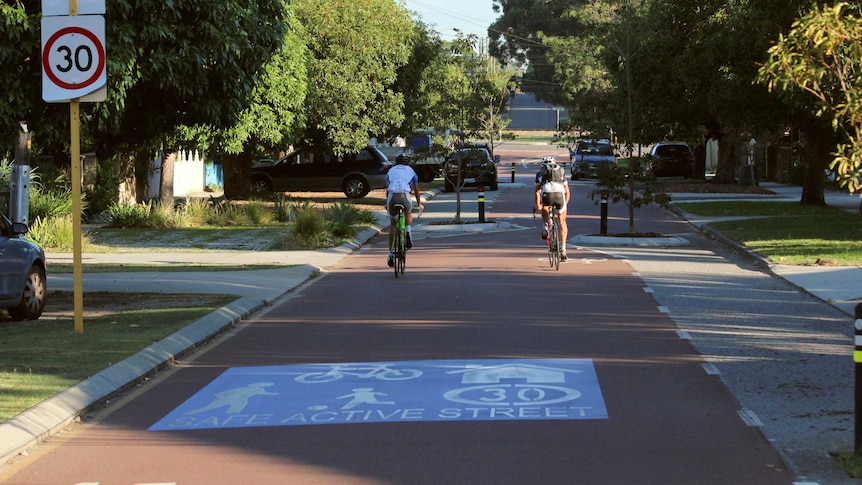 Two cyclists ride down a shady street where bicycles are given traffic priority