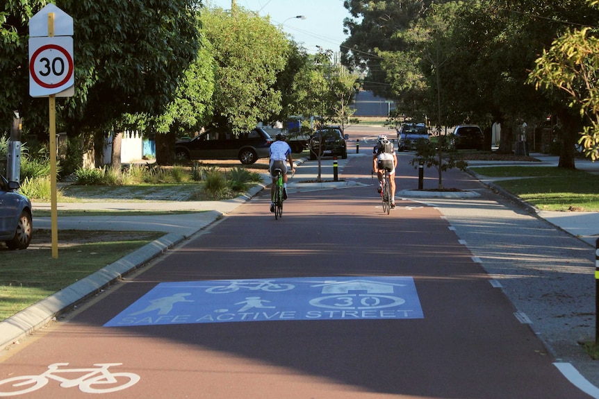 Two cyclists ride down a shady street where bicycles are given traffic priority