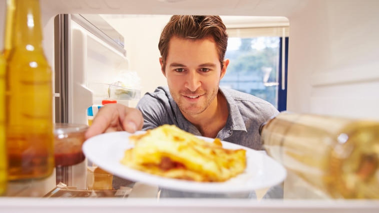 A man looking into a fridge for leftovers