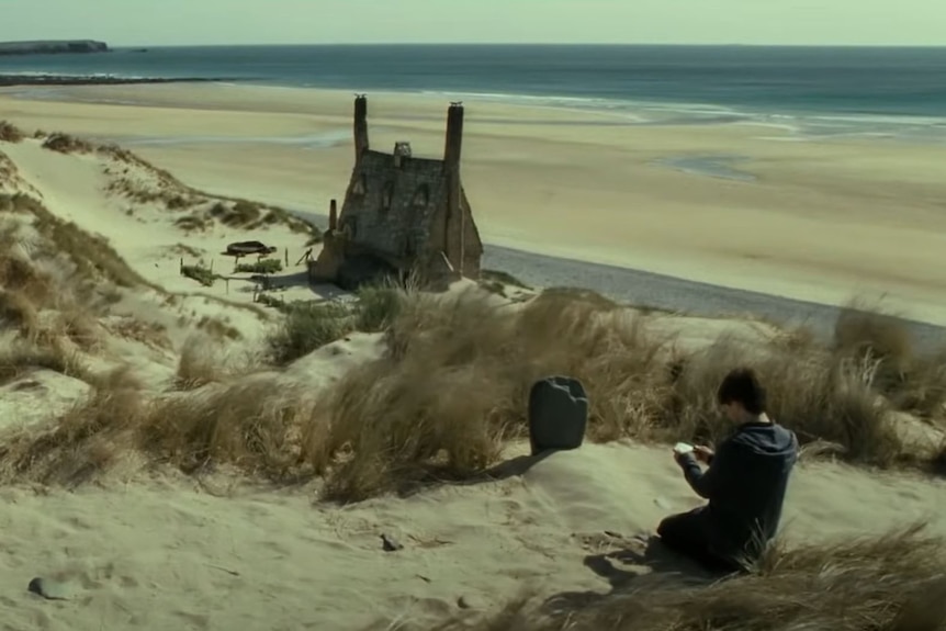 Harry Potter sits at the grave of Dobby the house elf on a sand dune overlooking Freshwater West beach. 