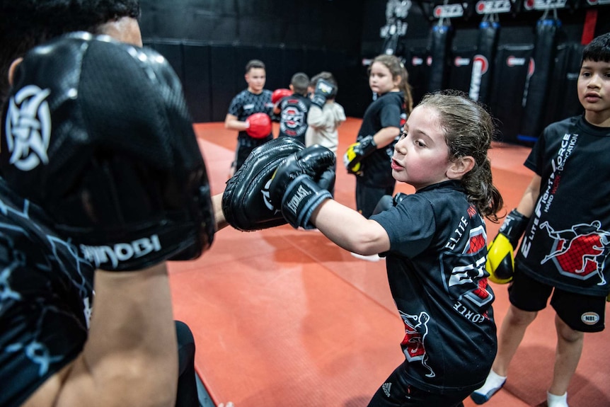 A boy punches the pad of his instructor using boxing gloves.