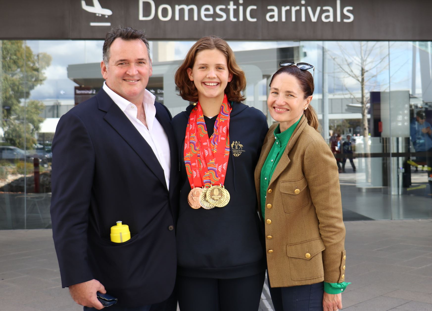 A young woman wearing many medals around her neck with an older person standing on either side of her.