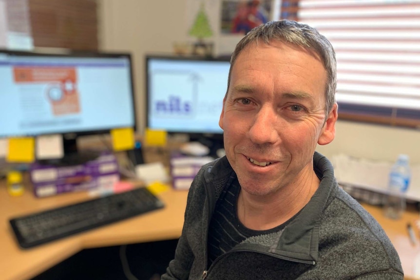 Man smiles at camera while sat at computer