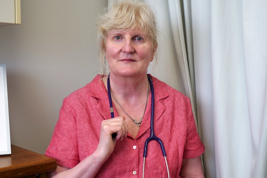 A doctor in a pink shirt holds her stethoscope 