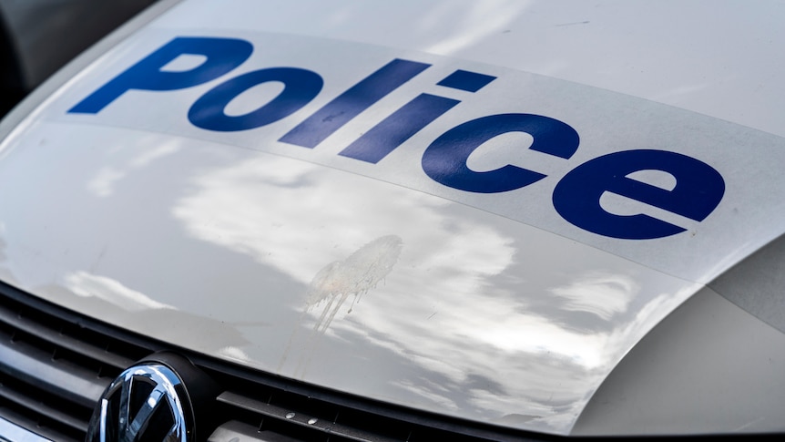The picture is a close up of a white police car's bonnet with the word police written in blue