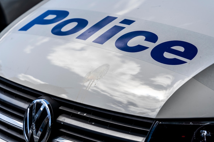 The picture is a close up of a white police car's bonnet with the word police written in blue