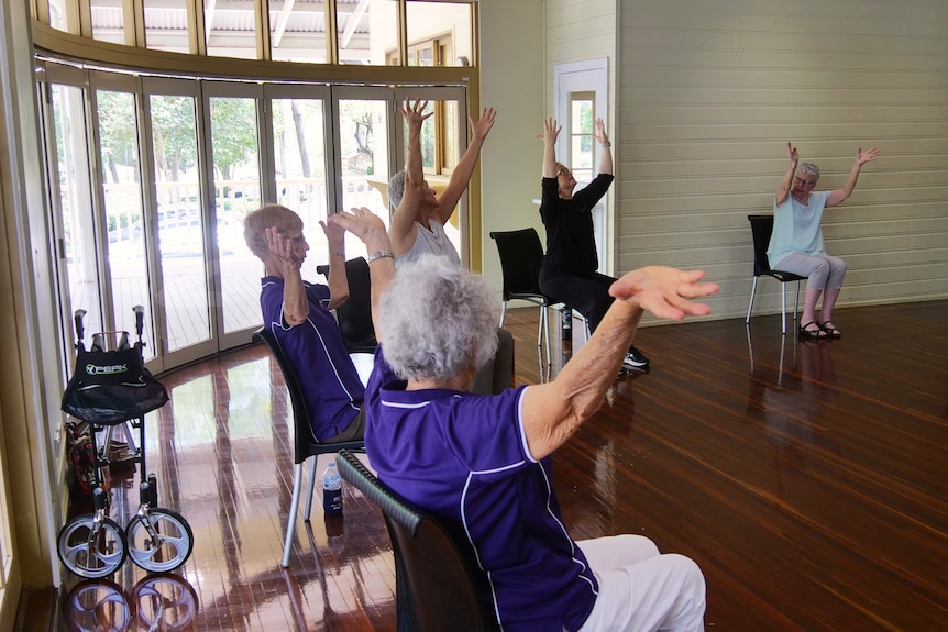 A group of woman sit on chairs in a circle with their arms raised in the air