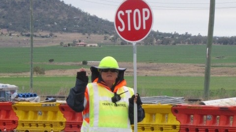 A woman wearing high-vis clothing holds a stop sign at a roadwork site.