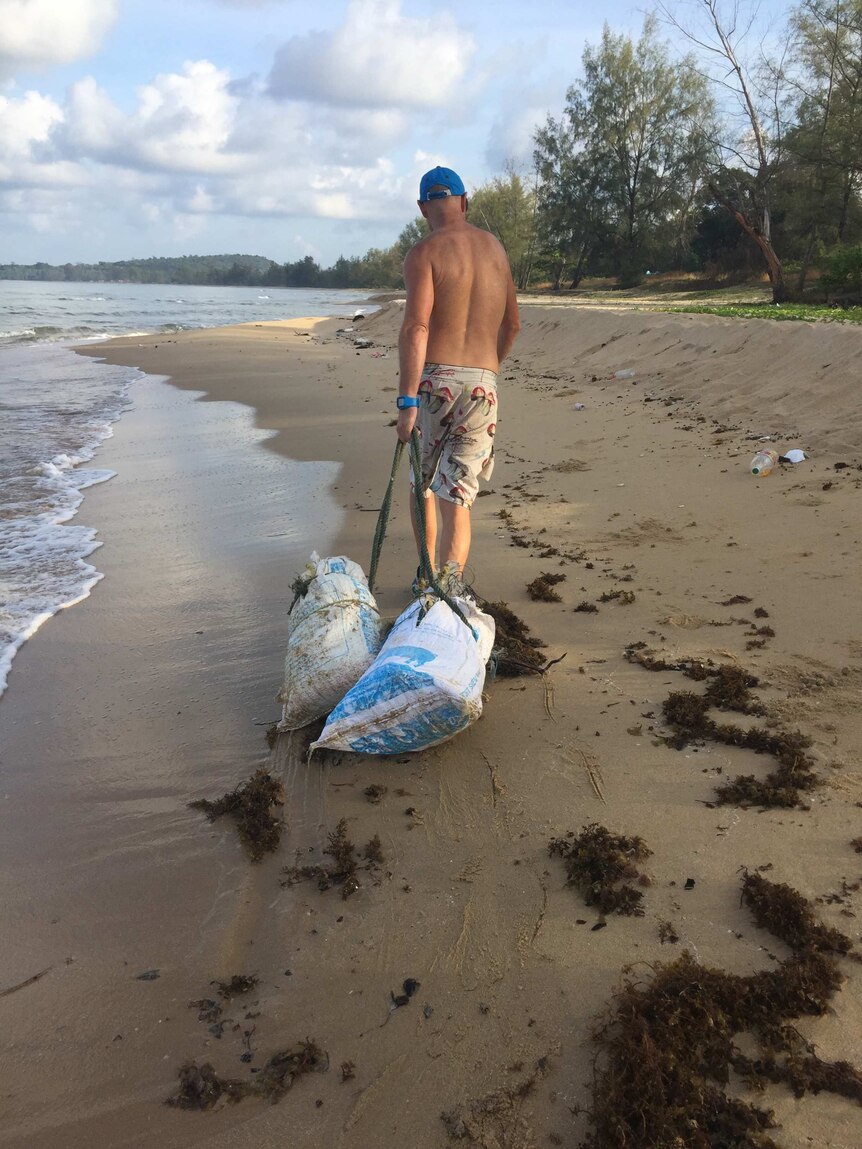 Paul Hellier drags two bags of rubbish on a beach.