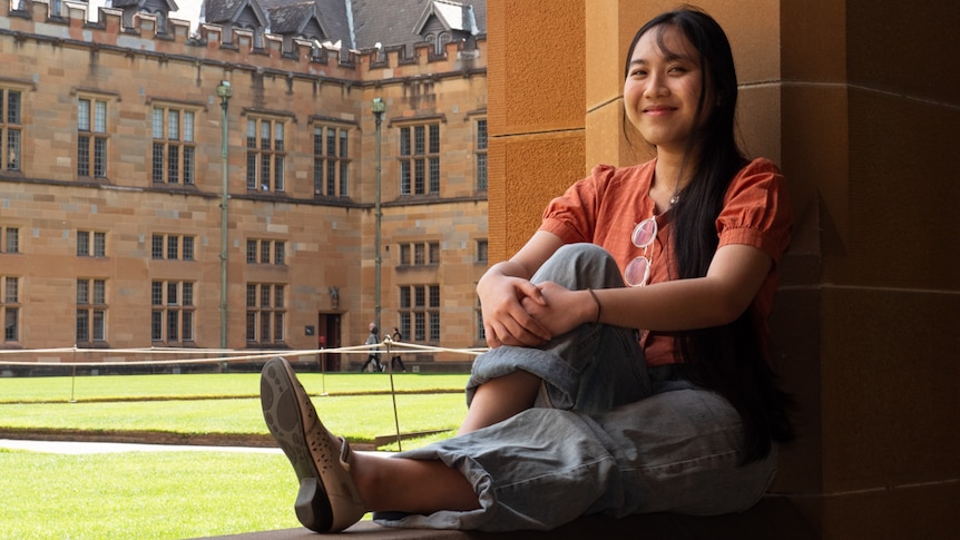 A female with black hair sits on a wall at Sydney University