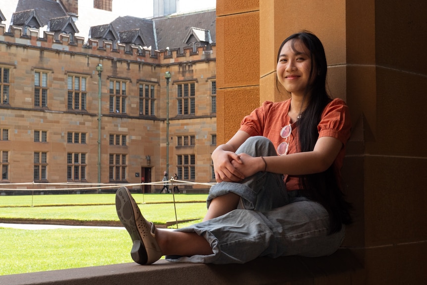 A female with black hair sits on a wall at Sydney University