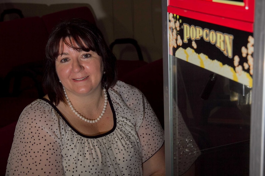 A woman in a darkened room with seats in the background and a popcorn machine at the front