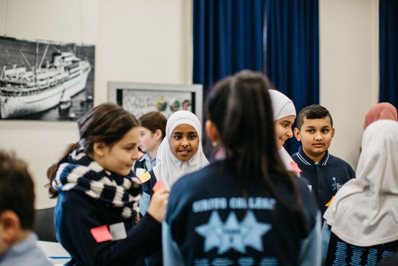 Young students in school uniforms stand talking to each other.