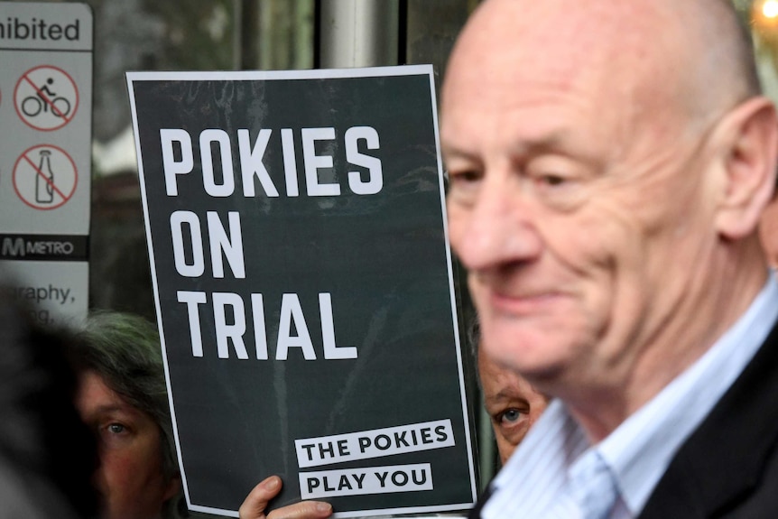 Australian Baptist minister Tim Costello stands next to a Pokies on Trial sign.