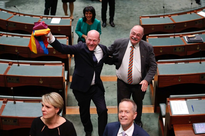 Trent Zimmerman, waving a rainbow flag and grinning from ear to ear, has his arm around Warren Entsch, wearing a rainbow tie