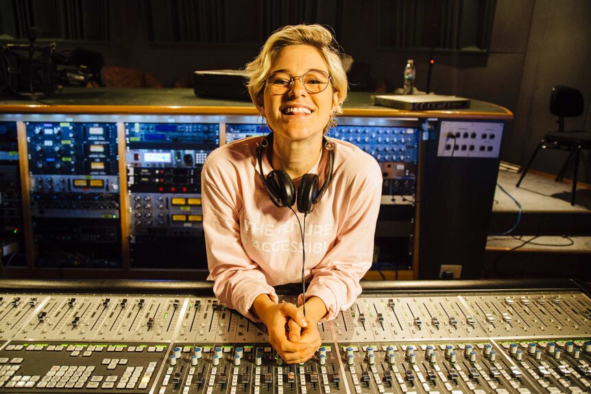 Elly Scrine sits in front of a panel in a recording studio.