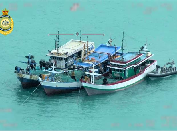 Três barcos maiores de madeira azul e um pequeno barco ancorados na água.