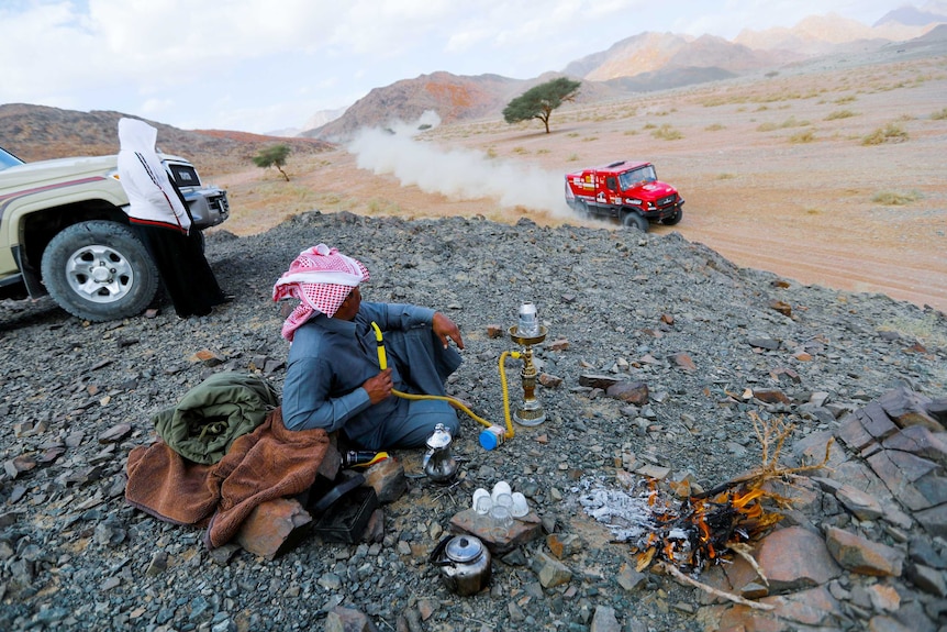 A man watches a race car drive past him in the desert