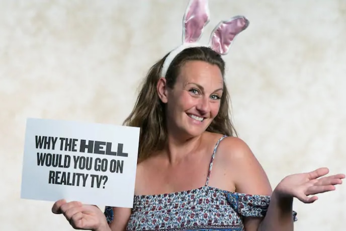 Sara-Marie Fedele holding a sign that says "Why the hell would you on reality TV?"