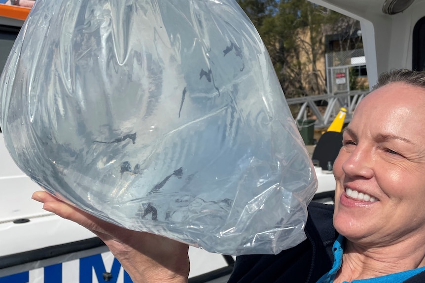 A smiling woman holds a large plastic bag.