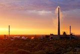 Sunset at a mining operation with a big smoke stack.  