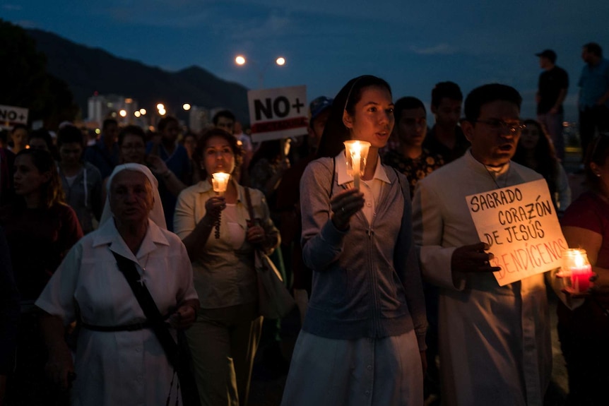 People march holding candles and signs.