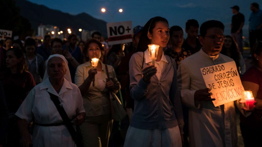 People march holding candles and signs.