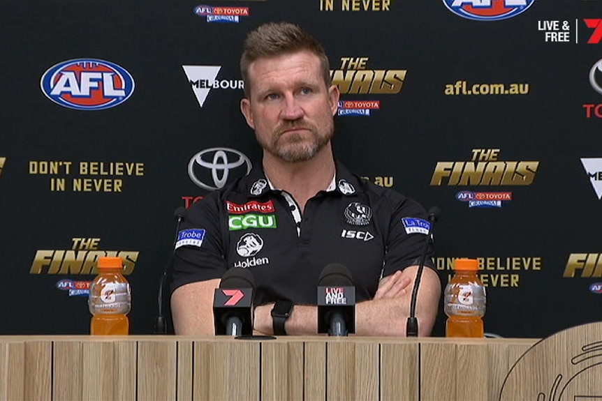 Nathan Buckley sits with folded arms looking up at the post-match press conference.