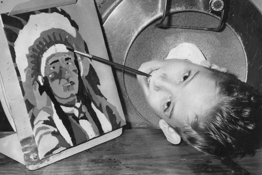Paul Alexander in his iron lung when he was young painting with a paintbrush in his mouth