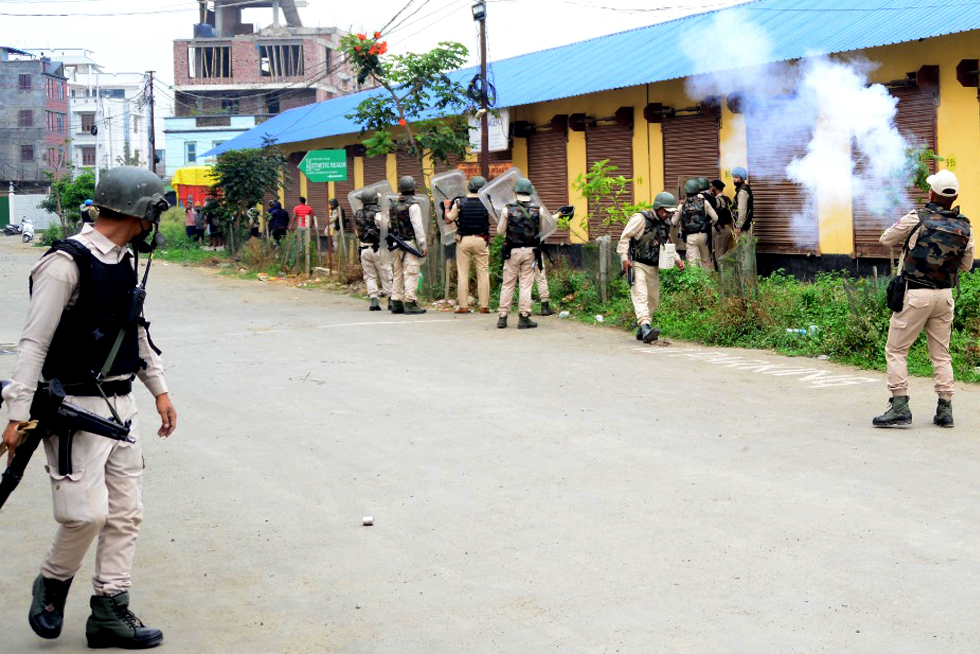 Security personnel fire tear gas while holding weapons in the street.