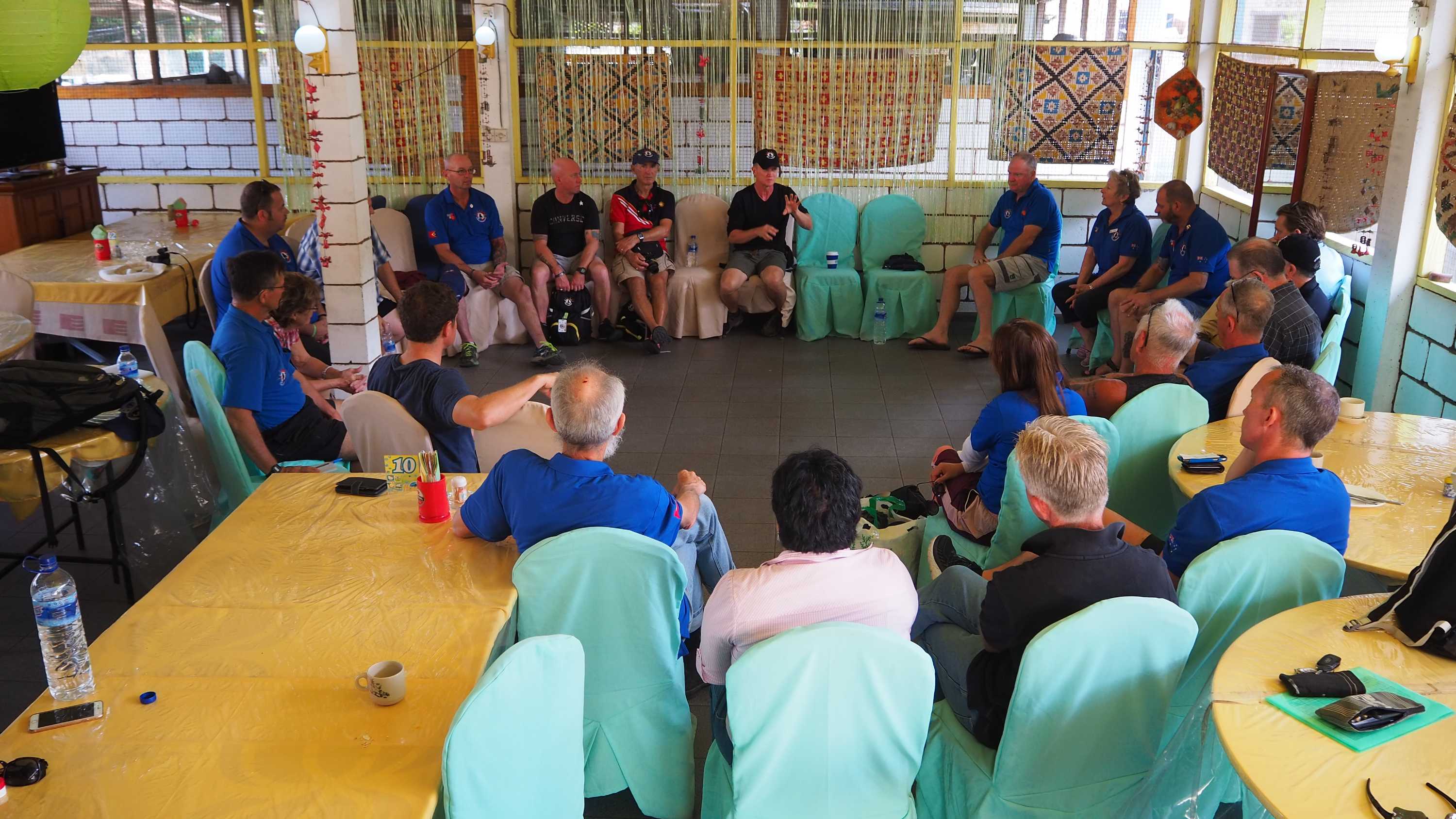 A large group of people sit in a circle on chairs