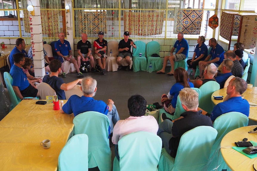 A large group of people sit in a circle on chairs