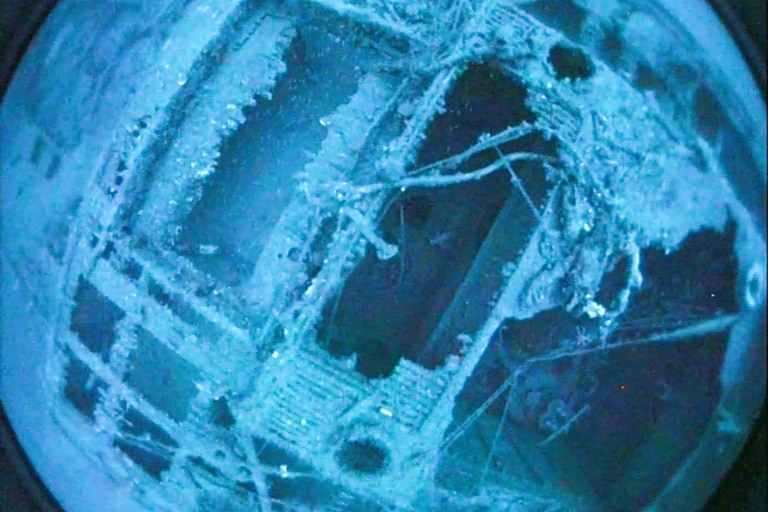 A close up shot of a shipwreck on the ocean floor, through footage from a drop camera