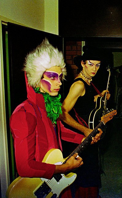 Un hombre con un traje extravagante, con un abrigo rojo, pintura en la cara y un mohawk. 