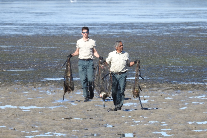 Two men carry what's left of pots across a mud flat.